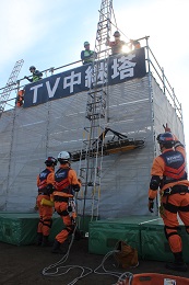 救助隊が高さ約ななメートルの建物の上階から負傷者を梯子とロープを使って救出している様子