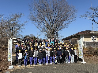 美の山公園の階段を使って全員で記念撮影している。両端に全国植樹祭の旗がある。空は冬晴れ。
