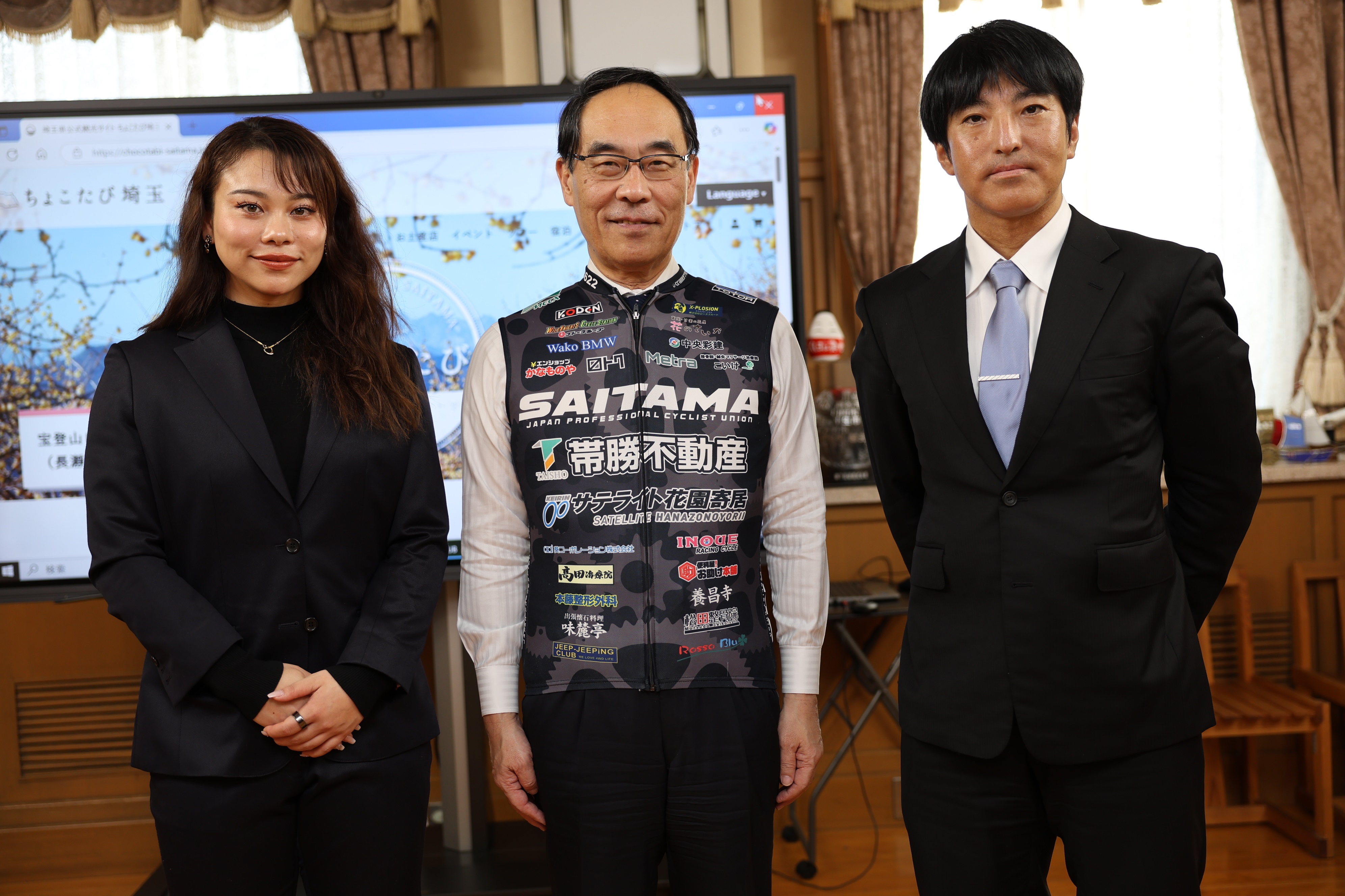 感謝状贈呈式で訪問者と記念撮影をする知事の写真(知事は競輪の格好をして)