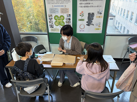 こども達が、職員の説明を聞きながら顕微鏡観察を行っている様子