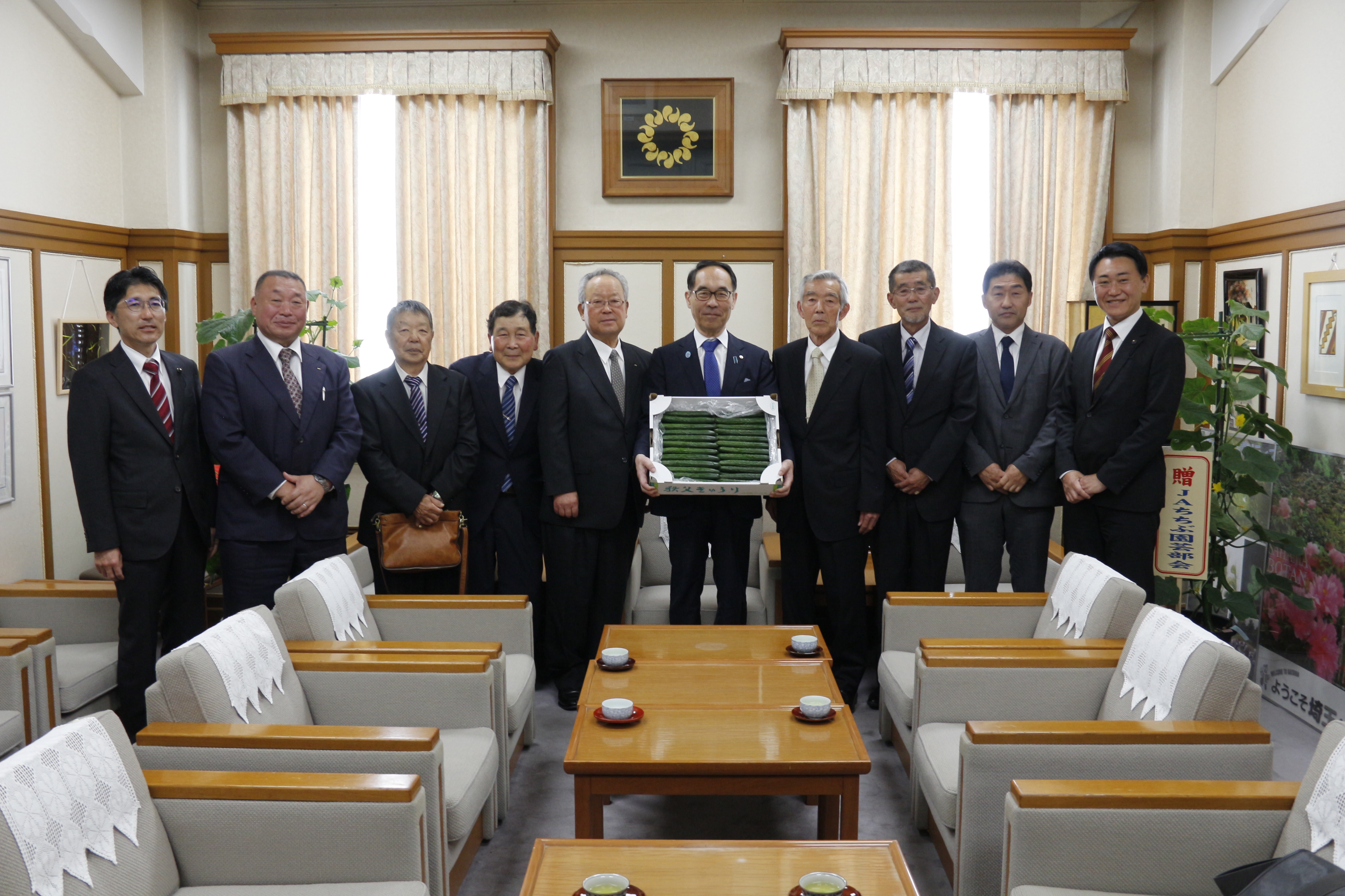 きゅうりを持ちながら訪問者と集合写真を撮る知事の写真