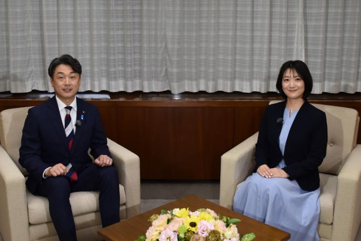 写真：横川議会運営委員長がアナウンサーと対面で座っている