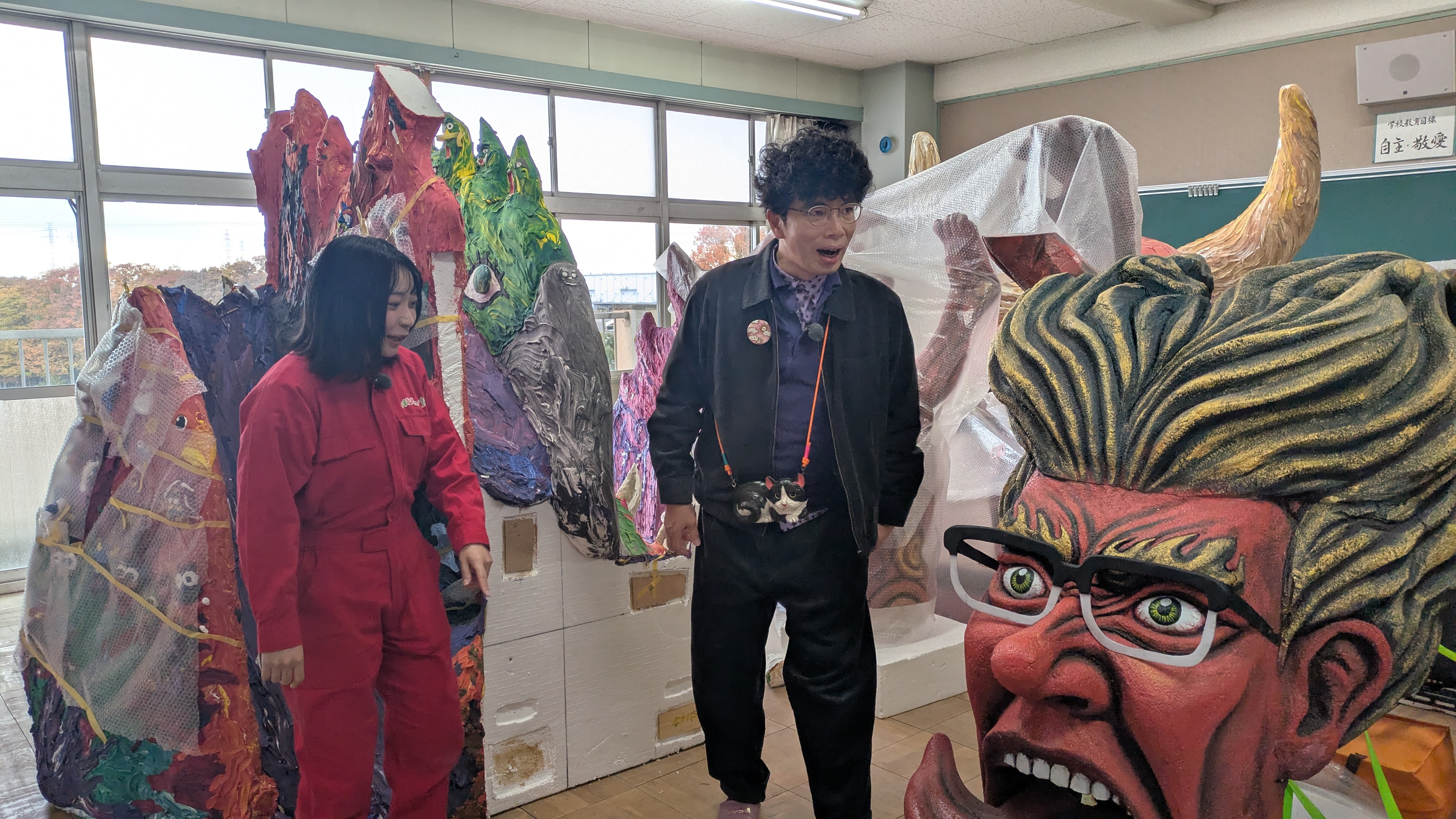 中学校の作品の前で話す片桐仁とアンゴラ村長